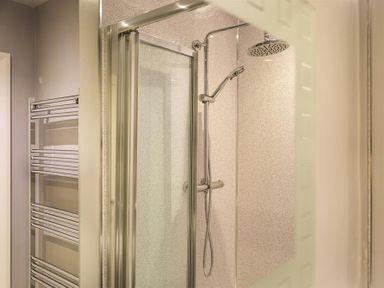 A shower cubicle with sliding glass door and a wall-mounted chrome shower head and handheld shower at Heathfield in Keswick
