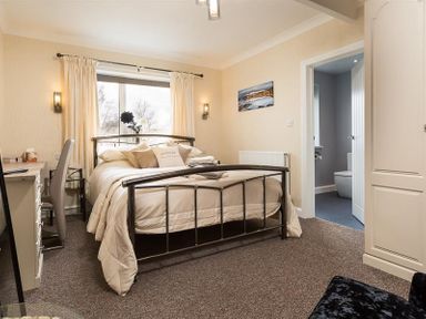 A bedroom with a double bed, desk, chair, window with curtains, and an open door leading to a bathroom at Heathfield in Keswick