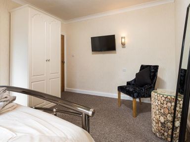 A bedroom with a double bed metal frame a white wardrobe a black chair with a pillow a stone side table and a wall mounted tv at Heathfield in Keswick