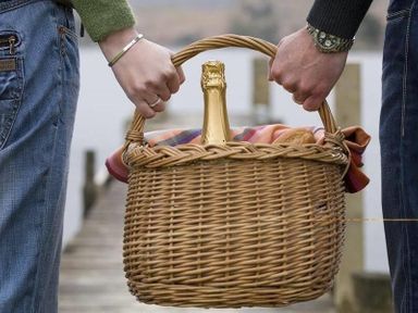Two people carrying a wicker basket with a bottle wrapped in a cloth on a wooden dock