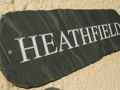A black stone plaque with the word Heathfield on a textured beige wall at Heathfield in Keswick