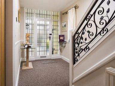 An entrance hall with a glass door window panel a wooden sculpture on a pedestal and a decorative wrought iron staircase railing at Heathfield in Keswick