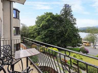A balcony with two black chairs and a small table overlooking trees a road and water at Pure Grace in Ambleside
