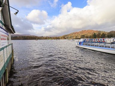 A lake with boats and a pier building with hills in the background at Pure Grace in Ambleside