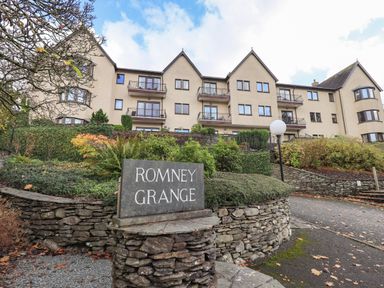 An exterior view of a multi-story residential building with balconies and a stone sign reading Romney Grange in front