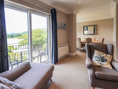 A sitting area with armchair and chaise lounge next to sliding glass doors with view outside and a dining table with chairs in the background at Pure Grace Ambleside