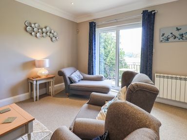 A living room with gray armchairs a side table with a lamp and sliding glass doors with blue curtains at Pure Grace in Ambleside