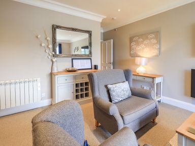 A living room with two grey armchairs a side table with a lamp a console table with a mirror and decorative items at Pure Grace Ambleside