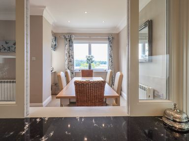 A dining room with a wooden table and six chairs with a window and floral curtains at Pure Grace in Ambleside