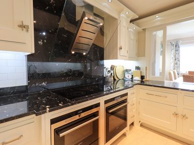 A kitchen with black marble countertops a glass stove hood two built in ovens and white cabinets at Pure Grace in Ambleside