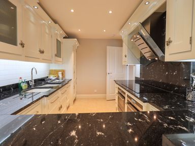 A galley kitchen with black marble countertops white cabinets and recessed lighting at Pure Grace in Ambleside