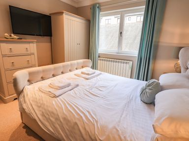 A bedroom with a bed with white linens folded towels a chest of drawers a wardrobe a wall-mounted TV and a window with curtains at Pure Grace in Ambleside