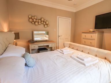 A bedroom with a bed towels on it a dressing table with a mirror a chest of drawers and a wall-mounted TV at Pure Grace in Ambleside
