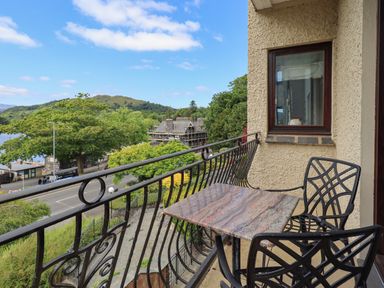 A balcony with a stone table and two metal chairs overlooking a road trees and hills at Pure Grace in Ambleside