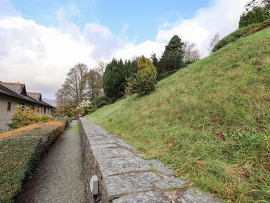 A pathway with hedges and stone wall next to a grassy slope with trees at Pure Grace in Ambleside