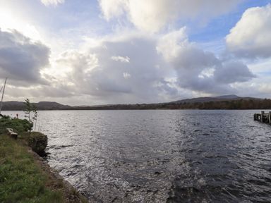 A view of a large body of water with trees and hills in the background and a cloudy sky at Pure Grace in Ambleside