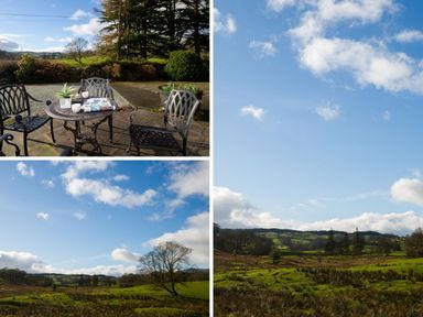 An outdoor patio with a table and chairs on a paved area overlooking a green landscape with trees and hills at Honister Cottage in Ambleside