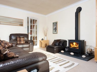 A living room with brown leather sofas a wood burning stove and a striped rug at Honister Cottage in Ambleside