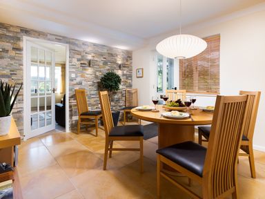 A dining room with a round wooden table set with plates glasses and a fruit bowl and wooden chairs with leather cushions at Honister Cottage in Ambleside