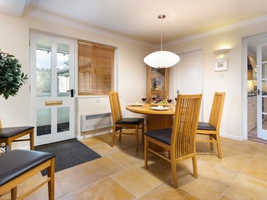 A dining area with four wooden chairs around a round table set for four people next to a glass door and window with blinds at Honister Cottage in Ambleside