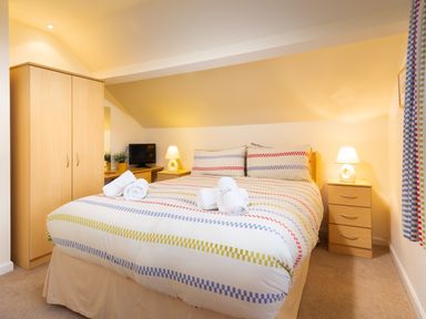A bedroom with a double bed with striped bedding bedside tables lamps a wardrobe a TV and curtains at Honister Cottage in Ambleside