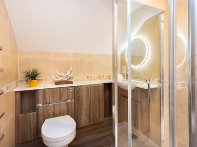 A bathroom with a toilet sink shower and wooden cabinets at Honister Cottage in Ambleside