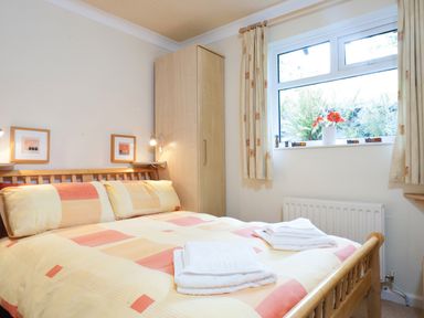 A bedroom with a double bed and folded towels on the bed near a window with curtains and a wardrobe at Honister Cottage in Ambleside