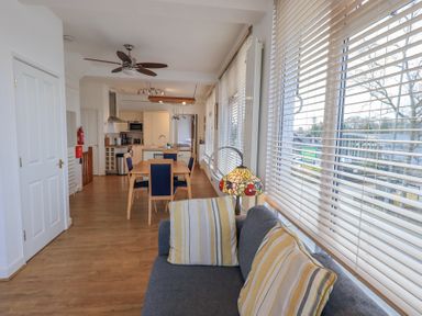 An open living and kitchen area with a dining table and chairs a ceiling fan and large windows with blinds at Windows Ambleside