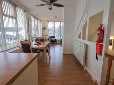 A dining area with wooden table and chairs next to large windows and a seating area with armchairs at Windows Ambleside