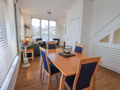 A dining area with a wooden table and blue chairs next to a living area with armchairs and a sofa at Windows in Ambleside