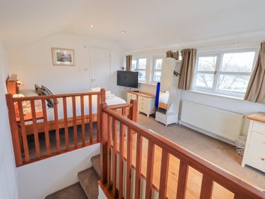 A bedroom with a wooden bed, television, dresser, mirror, and windows at Windows in Ambleside