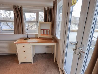 A wooden desk with drawers and a mirror on top beside windows and a glass door at Windows in Ambleside