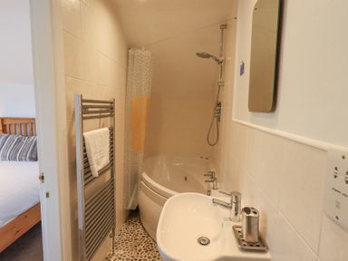 A small bathroom with a bathtub shower combination a sink a metal towel rack and a mirror at Windows Ambleside
