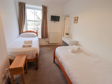 A bedroom with two single beds a small wooden table a wall-mounted television and a white desk with a plant at Windows Ambleside