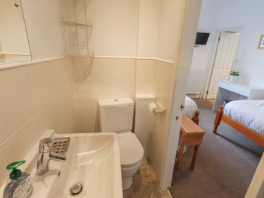 A bathroom with a sink, toilet, and wall-mounted shelf next to a bedroom with twin beds and a wooden bench at Windows in Ambleside