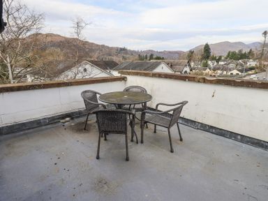 A rooftop patio with a round table and four wicker chairs overlooking a residential area and hills at Windows in Ambleside