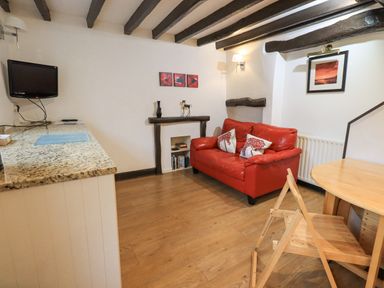 A small living room with a red sofa and wooden folding chair next to a round table and a wall-mounted TV at Cobblestone Cottage in Ambleside