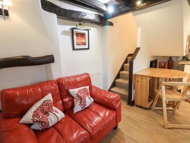 A red leather sofa with two tree patterned pillows near a small wooden dining table and staircase at Cobblestone Cottage in Ambleside