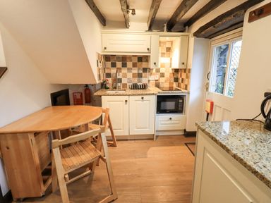 A kitchen with wooden table and chairs microwave sink and tiled backsplash at Cobblestone Cottage Ambleside
