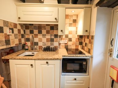 A kitchen area with a sink a stove a microwave and tiled backsplash at Cobblestone Cottage in Ambleside