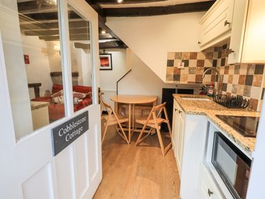 A kitchen with a wooden round table and chairs a tiled backsplash and granite countertops at Cobblestone Cottage Ambleside