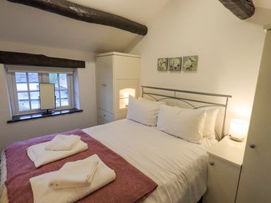 A bedroom with a double bed bedside tables a lamp and a window at Cobblestone Cottage in Ambleside