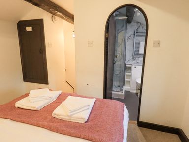 A bedroom with a bed with folded towels and a view through an arched doorway into a bathroom at Cobblestone Cottage in Ambleside
