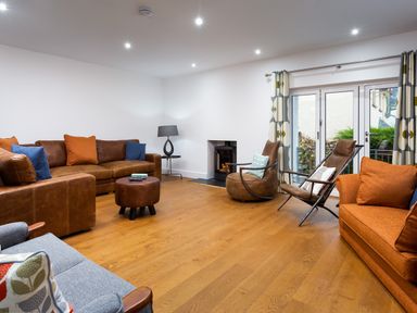 A living room with brown leather sofas orange pillows blue pillows a gray armchair a round ottoman a fireplace and glass doors with patterned curtains at Wynford in Ambleside