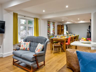 A living area with a grey loveseat and colorful cushions next to a dining table with multicolored chairs at Wynford in Ambleside