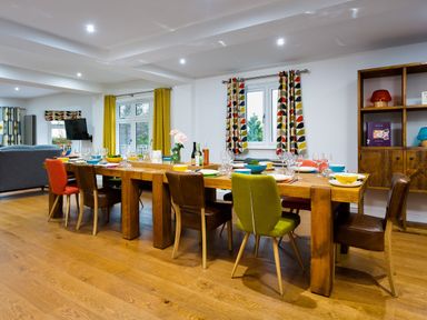 A dining room with a long wooden table set with dishes and glasses and various chairs around it at Wynford in Ambleside