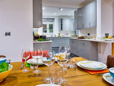 A dining table set with plates and wine glasses in a kitchen with gray cabinets and countertop at Wynford in Ambleside