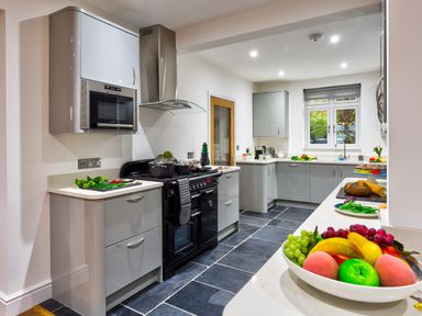 A kitchen with grey cabinets, a black stove, countertop appliances, and bowls of fruit at Wynford in Ambleside