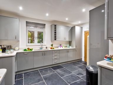 A kitchen with grey cabinets black tiled floor and kitchen utensils near a window at Wynford in Ambleside