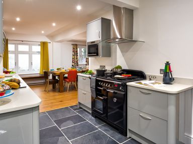 A kitchen with black stove gray cabinets and a dining table with chairs by windows with yellow curtains at Wynford in Ambleside
